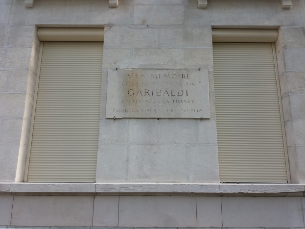 Ein zweistöckiges Gebäude mit zwei Fenstern, jeweils mit Läden, und einer Gedenktafel an seiner Seite.