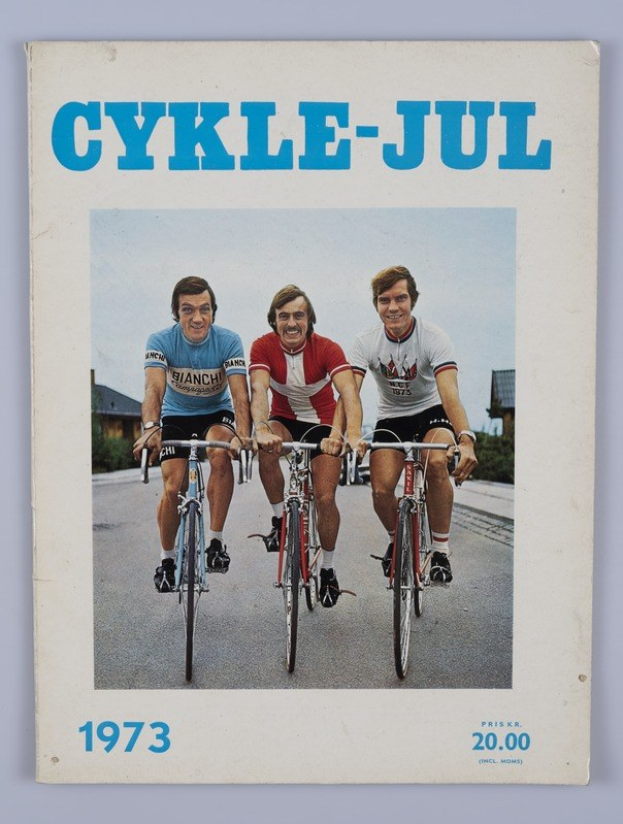 Drei Menschen auf Fahrrädern auf einer Straße mit Häusern, Bäumen und einem klaren blauen Himmel, mit \"Cykle-Jul 1973 - Cyclocross Magazine\"-Text oben und unten.