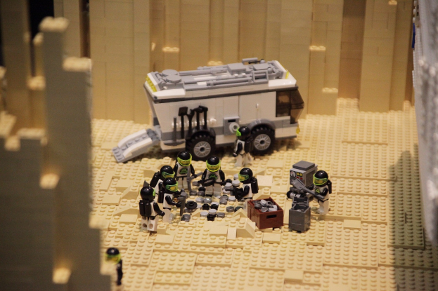 Lego-Modell einer Star Wars-Szene mit einem Gel├Ąndefahrzeug im Vordergrund und verstreuten Spielzeugen sowie einer Wand im Hintergrund.
