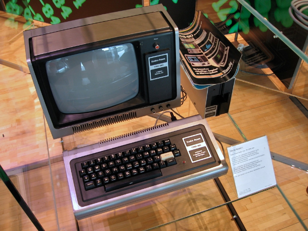 Ein Computersystem auf einem Glastisch mit einer Platte davor, Broschüren auf der CPU und einem Holzboden im Hintergrund.