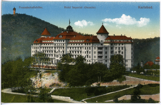 Alte Ansichtskarte des Hotels Imperial in Karlsbad, Deutschland, zeigt ein großes Gebäude mit Fenstern, umgeben von Bäumen, Pflanzen, einem Weg, Hügeln und einem bewölkten Himmel mit Text oben.