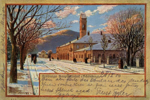 Ein altes Postkartenmotiv zeigt ein schneebedecktes Gebäude umgeben von Bäumen, Menschen und einem Zaun, mit der Aufschrift "Freiburg Hauptbahnhof" unten.