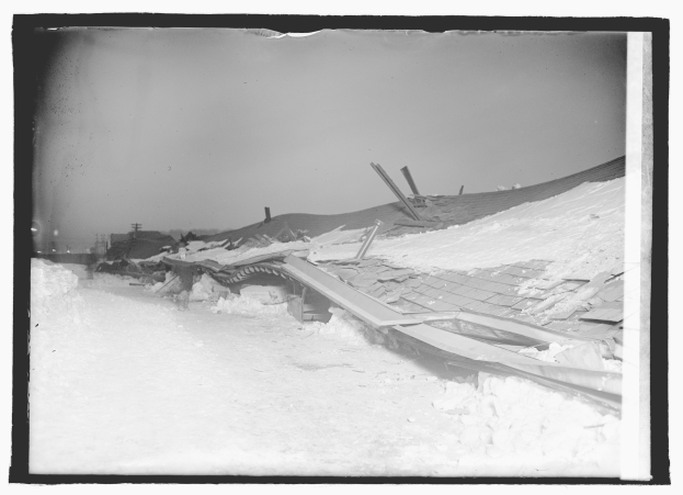 Ein Schwarz-Weiß-Foto eines abgerissenen Dachs mit schneebedeckter Erde und Pfählen im Hintergrund.