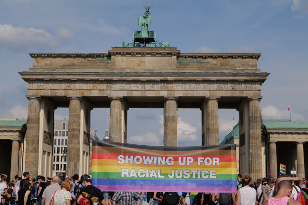 Eine Gruppe von Menschen steht vor dem Brandenburger Tor in Berlin, Deutschland, und hält ein Transparent mit der Aufschrift "Racial Justice."