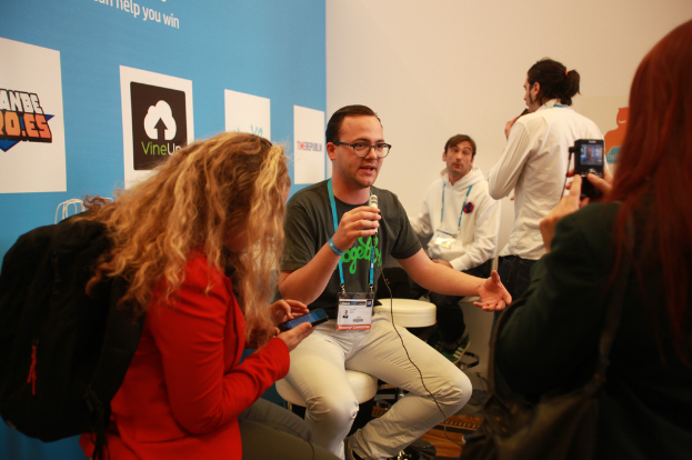 Ein Interview findet mit Menschen mit Mikrofonen und einer Kamera statt, mit Personen im Vordergrund und einem Banner links und einem klaren Hintergrund.