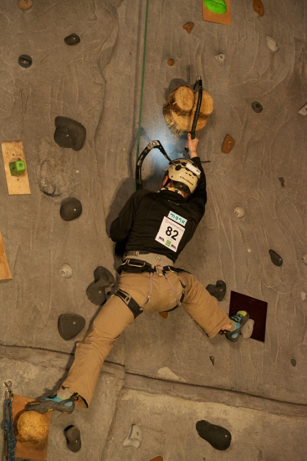 Eine Person in einem Helm klettert drinnen und hält ein Kletterwerkzeug.