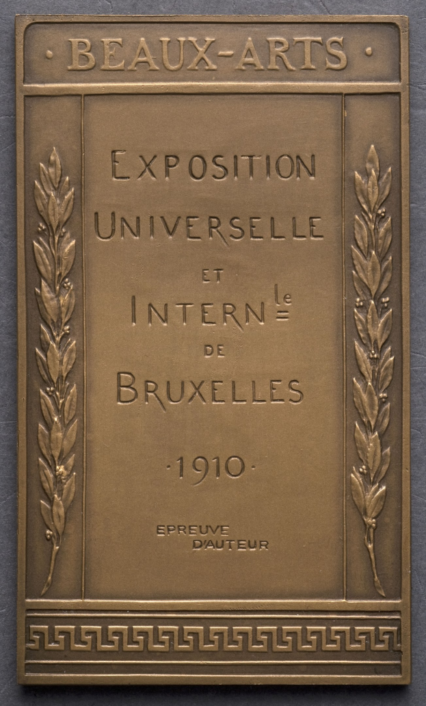 Bronzeplatte mit der Inschrift "Exposition Universelle et Internationale de Bruxelles 1910" in fetter Schrift, umgeben von einem dekorativen Rahmen und mit einem Glanzfinish.