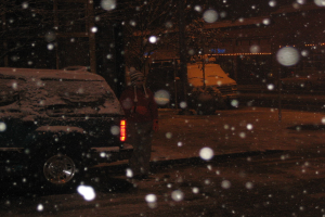 Eine dunkle Szenerie mit Schneefall und zwei Fahrzeugen auf einer Straße.
