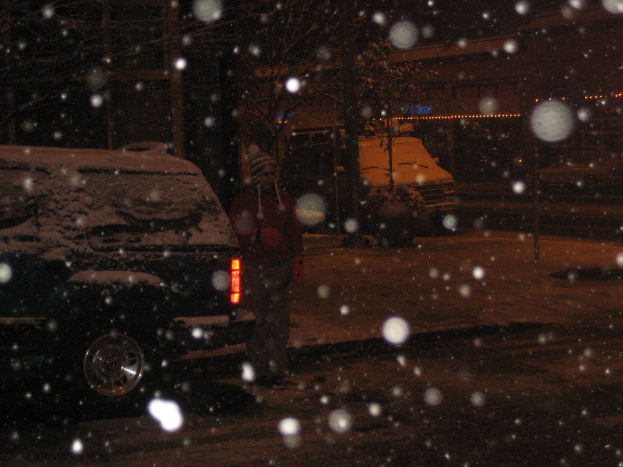 Eine dunkle Szenerie mit Schneefall und zwei Fahrzeugen auf einer Straße.