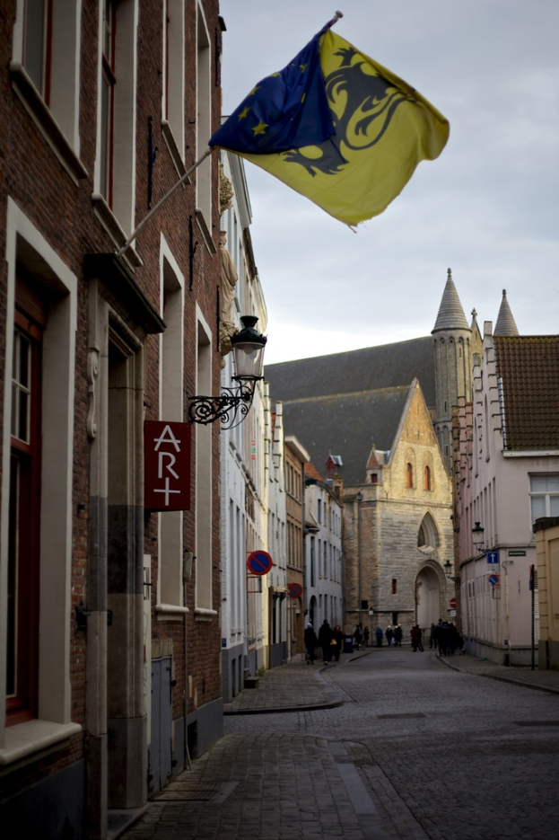 Eine Stadtansicht mit Gebäuden, Menschen auf der Straße, Polen, Schildern und einer Flagge an einem der Gebäude, mit dem Himmel darüber und der Straße darunter.
