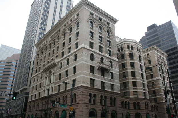 Gebäude mit Verkehrsampeln, Richtungsschildern und Fahnen im Vordergrund, mit einer Straßenlaterne und einer Tafel in der rechten unteren Ecke.
