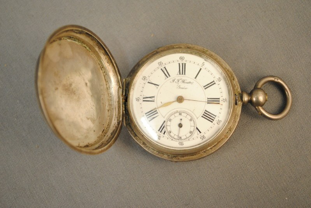 Eine silberne Taschenuhr mit einem weißen Zifferblatt mit römischen Ziffern auf einer grauen Oberfläche, mit einem Deckel für einen klassischen Look.