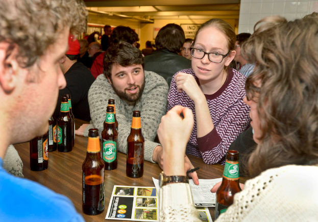 Mehrere Personen auf beiden Seiten eines Tisches mit Bierflaschen, die sich scheinbar in einer Bar befinden.