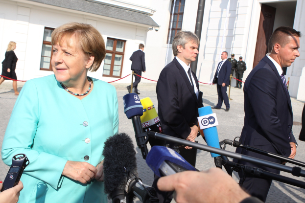 Bundeskanzlerin Angela Merkel beim Sprechen mit Reportern vor dem Kanzleramt in Berlin, umgeben von Menschen mit Mikrofonen und Gebäuden im Hintergrund.