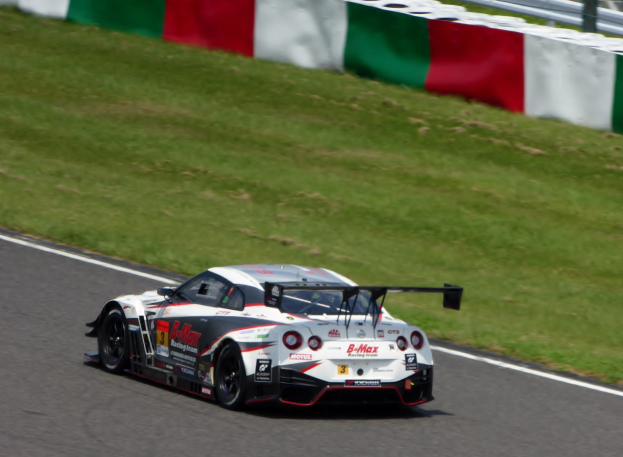 Ein Nissan GT-R Nismo GT3 Rennwagen auf der Nürburgring 24 Stunden Strecke, mit grünem Gras und einem Zaun im Hintergrund.