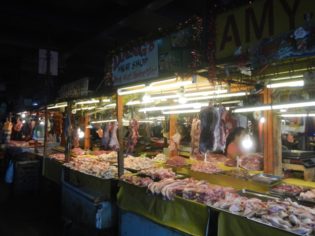 Ein nächtliches Metzgergeschäft mit beleuchteten Fleischauslagen, einige Kunden, eine Waage auf der rechten Seite und eine Hintergrundtafel.