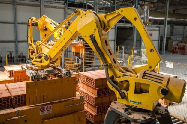 Große industrielle Lagerhalle mit gestapelten Kisten, Kränen an der Decke, Zaun, Strommasten und einer entfernten Wand in einer Herstellungsumgebung.