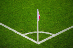 Ein Fußballfeld mit grünem Rasen, weißen Begrenzungslinien und einem weißen Pfosten mit einer roten und weißen Flagge auf dem zentralen Strafstoßpunkt.