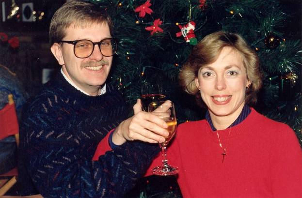 Ein Paar lächelt beim Halten von Weingläsern mit einem Weihnachtsbaum im Hintergrund.