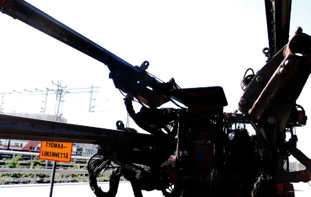 Eine Maschine ist im Vordergrund mit Strommasten, Kabeln, Barrieren, Pflanzen und Himmel im Hintergrund zu sehen.