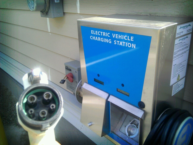 Elektrische Ladestation für Fahrzeuge, die an der Seite eines Gebäudes montiert ist, mit einem angeschlossenen Ladekabel und zusätzlichen an der Wand befestigten Gegenständen im Hintergrund.