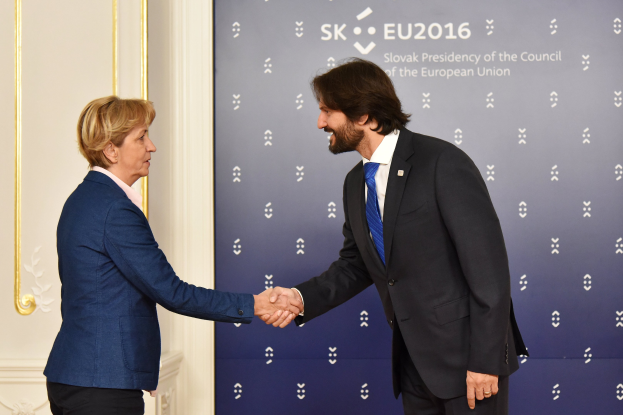 Bundeskanzlerin Angela Merkel und Bundeskanzler Joachim Gauck schütteln sich die Hände vor einer Wand mit einem "EU-Gipfel"-Banner und einer Tür im Hintergrund, beide lächeln.