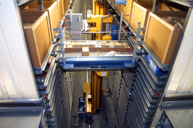 Großes Lagerinnere mit zahlreichen gestapelten Kartonagen, Industriegeräten und diverser Ausrüstung auf einem sichtbaren Boden.