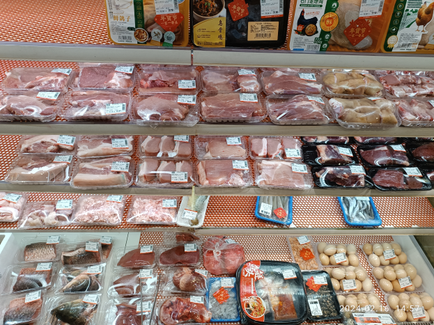 Eine Supermarkttheke voller verschiedener Fleischsorten in Plastikboxen, andere Lebensmittel und Preisschilder.