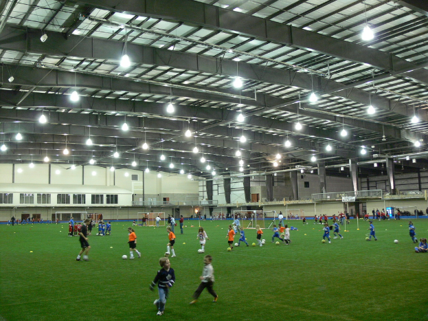 Eine Indoor-Fußballhalle mit einer Gruppe von Menschen, die mit einem Fußball auf dem Boden spielen, Torpfosten und Beleuchtung auf dem Dach.