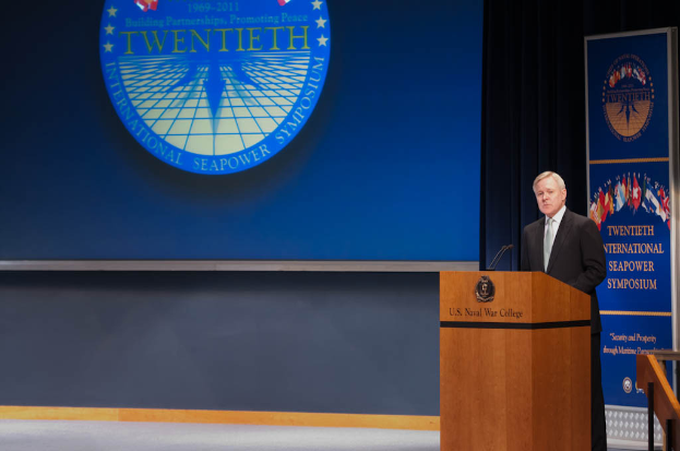 US-Außenminister Mike Pompeo, gekleidet in eine schwarze Jacke, weißes Hemd und schwarze Krawatte, steht an einem Podium mit zwei Mikrofonen, spricht bei der 20. Internationalen Seemacht-Symposium vor einem blauen Bildschirm und einem Geländer auf der rechten Seite.