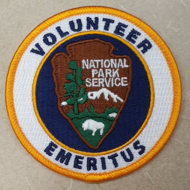 Runder Flicken mit blauem Rand und weißem Hintergrund, der schwarzen Text "Volunteer National Park Service Emeritus" in der Mitte eines gelben Kreises zeigt.