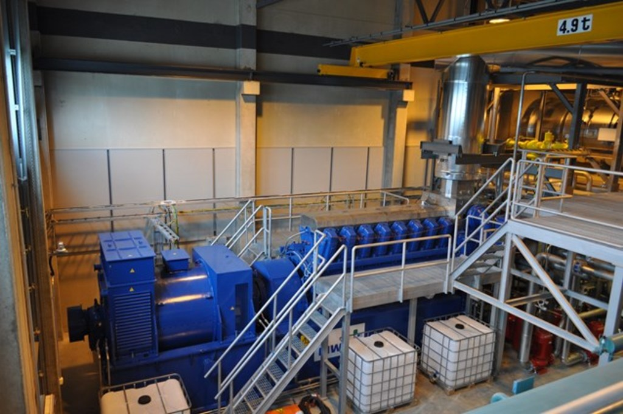 Ein Fabrikinnenraum mit TrÃ¤gern, einer Treppe mit GelÃ¤nder, Containern, Lichtern, Rohren und WÃ¤nden.