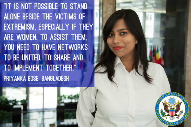 Eine Frau in einem weißen Hemd vor einem Gebäude mit einem Zitat über Einheit gegen Extremismus, ein Logo in der rechten unteren Ecke.