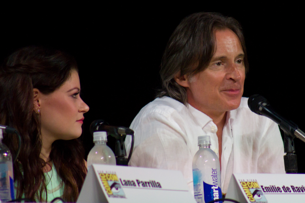 Ein Mann spricht in ein Mikrofon, während eine Frau neben ihm steht, vor einer Namensschilder und Wasserflaschen.