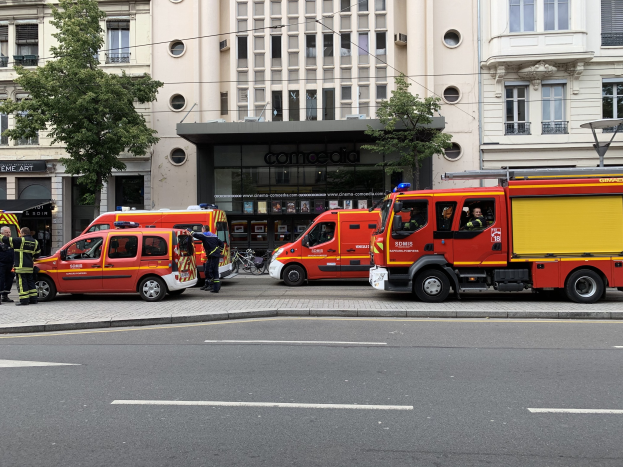 Eine Gruppe von Feuerwehrautos auf einer Straße in Paris geparkt, mit Menschen in der Nähe und Gebäuden, Bäumen und einem Fahrrad im Hintergrund.