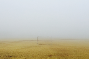 Ein Fußballtor steht in der Mitte eines Feldes, umgeben von dickem Nebel, mit dem Himmel darüber.