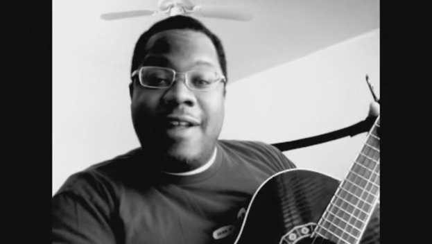 Ein Mann mit Brille spielt Gitarre, während über ihm ein Ventilator positioniert ist.