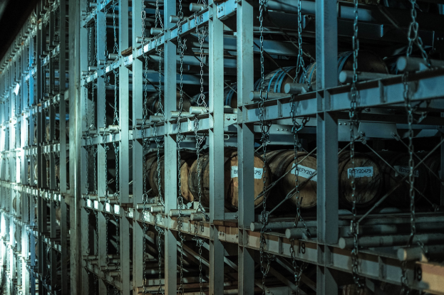 Großes Lagerhaus mit zahlreichen Fässern, die in Metallregalen gestapelt und durch Stangen und Ketten verbunden sind.