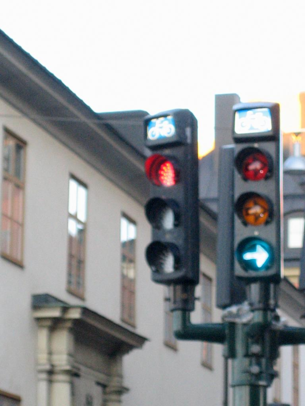 Ein Gebäude mit Fenstern auf der linken Seite und Verkehrsampeln mit einem Mast auf der rechten Seite.
