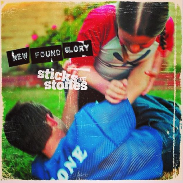 Zwei Personen sind in einen Kampf auf einem grasbewachsenen Gebiet mit Logos im Hintergrund verwickelt.