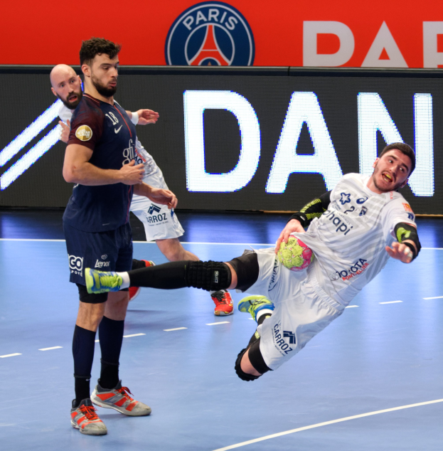 Eine Gruppe von Männern, die auf einem Handballfeld spielen, wobei einer den Ball hält, und ein Paris Saint-Germain-Futsal-Siegesschild im Hintergrund.