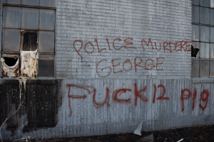 Ein Gebäude mit Graffiti, das "Polizei ermordet George Fuck 12 P19" auf der Seite trägt, mit Fenstern und verschiedenen Gegenständen vorne drauf.