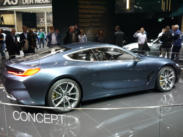 Ein BMW 8er-Konzeptfahrzeug mit glänzender schwarzer Lackierung und Chromakzenten wird auf der IAA in Frankfurt gezeigt, umgeben von Menschen, die Fotos machen, mit einem hell erleuchteten Hintergrund und einer Texttafel.