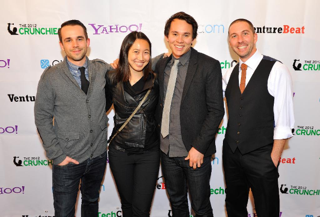 Eine Gruppe strahlender Individuals, die für die Kamera posieren, mit einem Sponsorenbanner im Hintergrund.