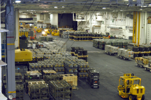 Ein großes Lagerinnere voller Numerous Trucks, Container, Menschen, Lichter, Stangen und andere Gegenstände mit einem prominenten Rad.