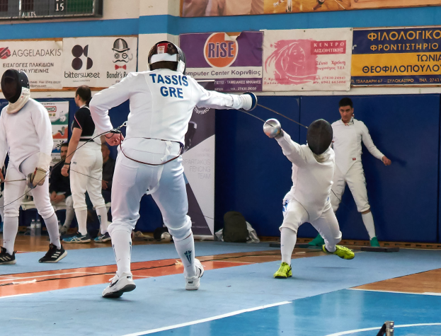 Eine Gruppe von Menschen, die in einer Turnhalle mit Bannern an der Wand und einer Anzeigetafel oben fechten, alle tragen Helme und halten Schwerter.