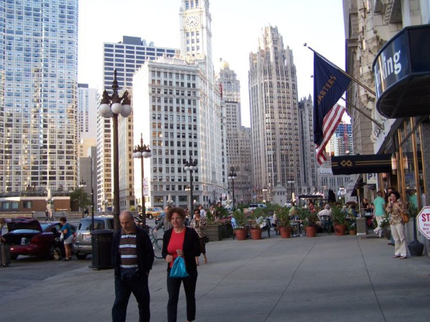Eine belebte StraßenSzene mit Menschen, Blumentöpfen, Autos, Straßenlaternen, Gebäuden, Geschäften und Flaggen auf der rechten Seite.