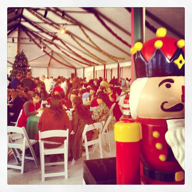 Eine Gruppe von Menschen feiert Weihnachten in einer Hütte mit einem geschmückten Baum, weißen Stühlen, einem roten Spielzeug-Sicherheitsmann und einer schwarzen Krone.