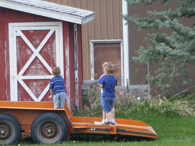 Ein Wagen mit Kindern darauf in der Mitte eines grasbewachsenen Bereichs, mit einem Baum und einem Haus im Hintergrund.