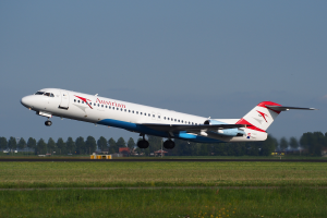 Ein Austrian-Airlines-Embraer-ERJ-190-Flugzeug beim Abheben vom Frankfurter Flughafen, mit grünem Gras, Bäumen und Gebäuden im Hintergrund und dem Himmel darüber.